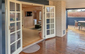 A wooden-floored interior with a large open door leading to a covered outdoor area with a table and chairs.