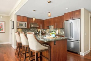 A modern kitchen with a central island, bar stools, stainless steel appliances, and pendant lighting. - Honua Kai | Ocean View 5 BR, Sleeps 14 | Car Incl. w/ 6+ Nights | HKK ML-3804 by KBM (Lahaina)