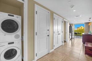A laundry room with Bosch washing machines, a kitchen area, and a view of a building through a glass door. - Honua Kai | Ocean View 5 BR, Sleeps 14 | Car Incl. w/ 6+ Nights | HKK ML-3804 by KBM (Lahaina)