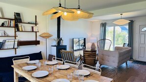 Uma sala de jantar com mesa de madeira posta para quatro pessoas, estante, lareira e vista para o exterior.