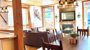 Un intérieur en bois comprenant une table à manger, des chaises, un canapé, une cheminée et un téléviseur.