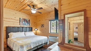 Ein Schlafzimmer einer Holzhütte mit Bett, Deckenventilator, Fenster und Spiegel.