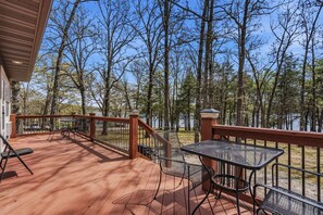 A wooden deck with outdoor furniture, a table, and chairs, overlooking a forested area. - Quail Cove Dogwood Lakefront Boat Slip Optional (Shell Knob)