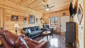 Interno di una baita in legno con divano, poltrona e televisore fissato al muro.