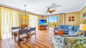 A spacious living room with a dining area, a large flat-screen TV, a ceiling fan, and a view of the outdoors. - Honua Kai | Ocean View 7 BR, Sleeps 20 | Car Incl. w/ 6+ Nights | HKK ML-3819 by KBM (Lahaina)