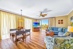 A spacious living room with a dining area, a large flat-screen TV, a ceiling fan, and a view of the outdoors. - Honua Kai | Ocean View 7 BR, Sleeps 20 | Car Incl. w/ 6+ Nights | HKK ML-3819 by KBM (Lahaina)