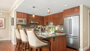 A modern kitchen with a central island, bar stools, stainless steel appliances, and pendant lighting. - Honua Kai | Ocean View 7 BR, Sleeps 20 | Car Incl. w/ 6+ Nights | HKK ML-3819 by KBM (Lahaina)