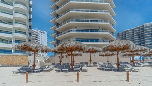 Ett hotell vid stranden med flera balkonger, solstolar och parasoller med halmtak.