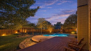 A backyard with a wooden deck, a swimming pool, and a wooden fence.