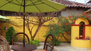 Une terrasse extérieure avec une table ronde et des chaises, un parasol vert et un mur jaune orné de fleurs rouges.