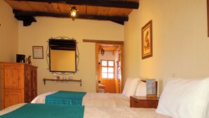 Une chambre avec un plafond en bois, un lit avec une literie blanche et turquoise, une commode en bois, un miroir et un tableau encadré au mur.