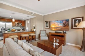 Eine moderne Küche mit Edelstahlgeräten, eine Bar, ein Wohnzimmer mit Sofa und Fernseher sowie ein Essbereich mit Tisch und Stühlen.