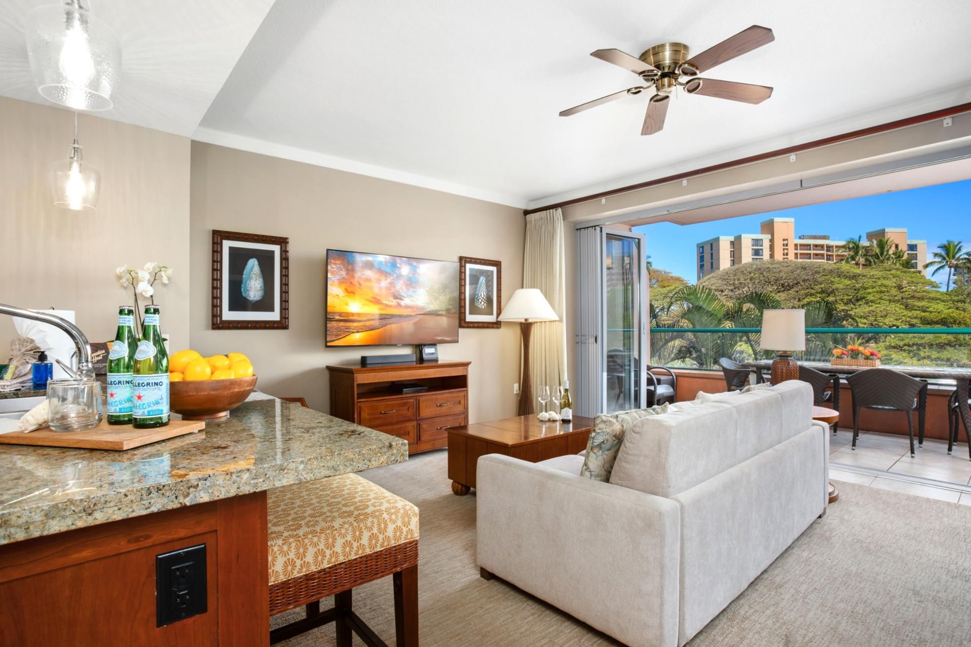 A modern hotel room with a kitchen area, a sofa, a dining table, and a balcony with a view of the city.