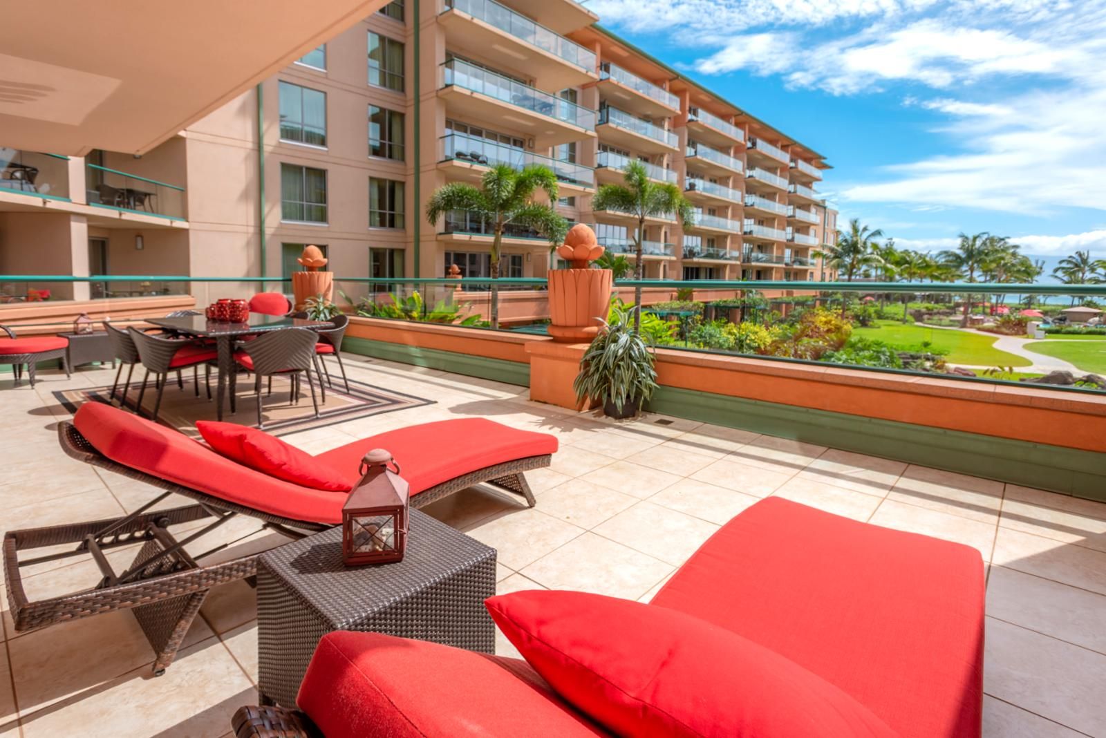 Un balcón de hotel con sillones reclinables rojos, una mesa y vistas al océano.