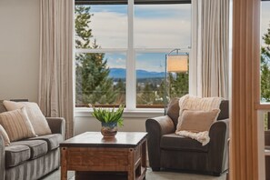 Un salon avec deux canapés, une table basse, une lampe et une vue sur les arbres et les montagnes, visible à travers une grande fenêtre.
