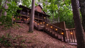 Eine Holzhütte mit einer Holztreppe, die zu einer Terrasse führt, umgeben von Bäumen.