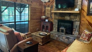 Ein Blockhaus-Innenraum mit Kamin aus Stein, einem darüber montierten Fernseher und einem großen Fenster.