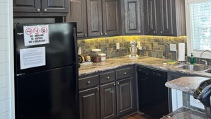 A kitchen with dark wooden cabinets, a black refrigerator, and a marble countertop. - Cozy cabin w/ hot tub near Beavers Bend (Broken Bow)