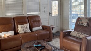 A spacious living room with a brown leather sofa, a wooden coffee table, and a ceiling fan. - Cozy cabin w/ hot tub near Beavers Bend (Broken Bow)