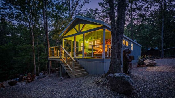 A cabin with a covered porch, a staircase leading to the entrance, and a large window. - Cozy cabin w/ hot tub near Beavers Bend (Broken Bow)