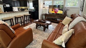 A living room with a brown leather sofa, a coffee table, and a television. - Cozy cabin w/ hot tub near Beavers Bend (Broken Bow)