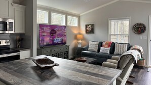 Uma cozinha moderna com televisão de tela plana, uma mesa de jantar e uma sala de estar aconchegante com sofá e mesa de centro.