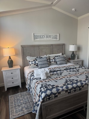 A bedroom with a bed, nightstands, a rug, and a sign on the wall. - Sassy Cowgirl: Hot Tub + Fire Pit by a Pond (Broken Bow)