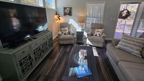 Uma sala de estar com televisão, dois poltronas, uma mesa de centro e um sofá.