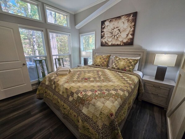 A bedroom with a large bed, a nightstand with a lamp, and a window with blinds. - Cozy cabin retreat w/ hot tub & fire pit (Broken Bow)