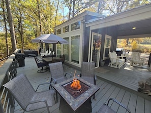 A covered deck with outdoor furniture, a fire pit, and a glass-enclosed patio area. - Cozy cabin retreat w/ hot tub & fire pit (Broken Bow)