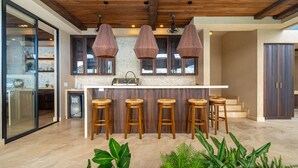 A modern kitchen with a central island, wooden stools, pendant lights, and a stone backsplash. - Riverstone – Elevated Living Near Beach & Town (Dominical)