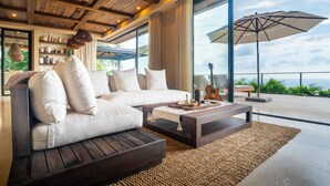 A modern living room with a sofa, coffee table, and large windows overlooking the ocean. - Riverstone – Elevated Living Near Beach & Town (Dominical)