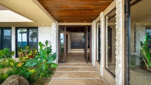 A stone pathway leading to a wooden door, surrounded by lush greenery and large plants. - Riverstone – Elevated Living Near Beach & Town (Dominical)
