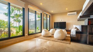 A modern living room with large windows, a flat-screen TV, and a cozy seating area with bean bags. - Riverstone – Elevated Living Near Beach & Town (Dominical)