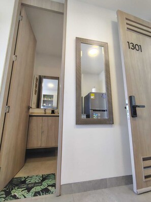 Ein Hotelzimmer mit einer Holztür mit der Aufschrift '1301', einem Spiegel mit verziertem Rahmen, einem kleinen Waschbecken und einer Toilette.