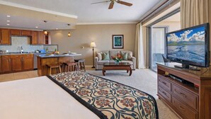 Ein Hotelzimmer mit Bett, Fernseher, Essbereich, Deckenventilator und einem großen Fenster.