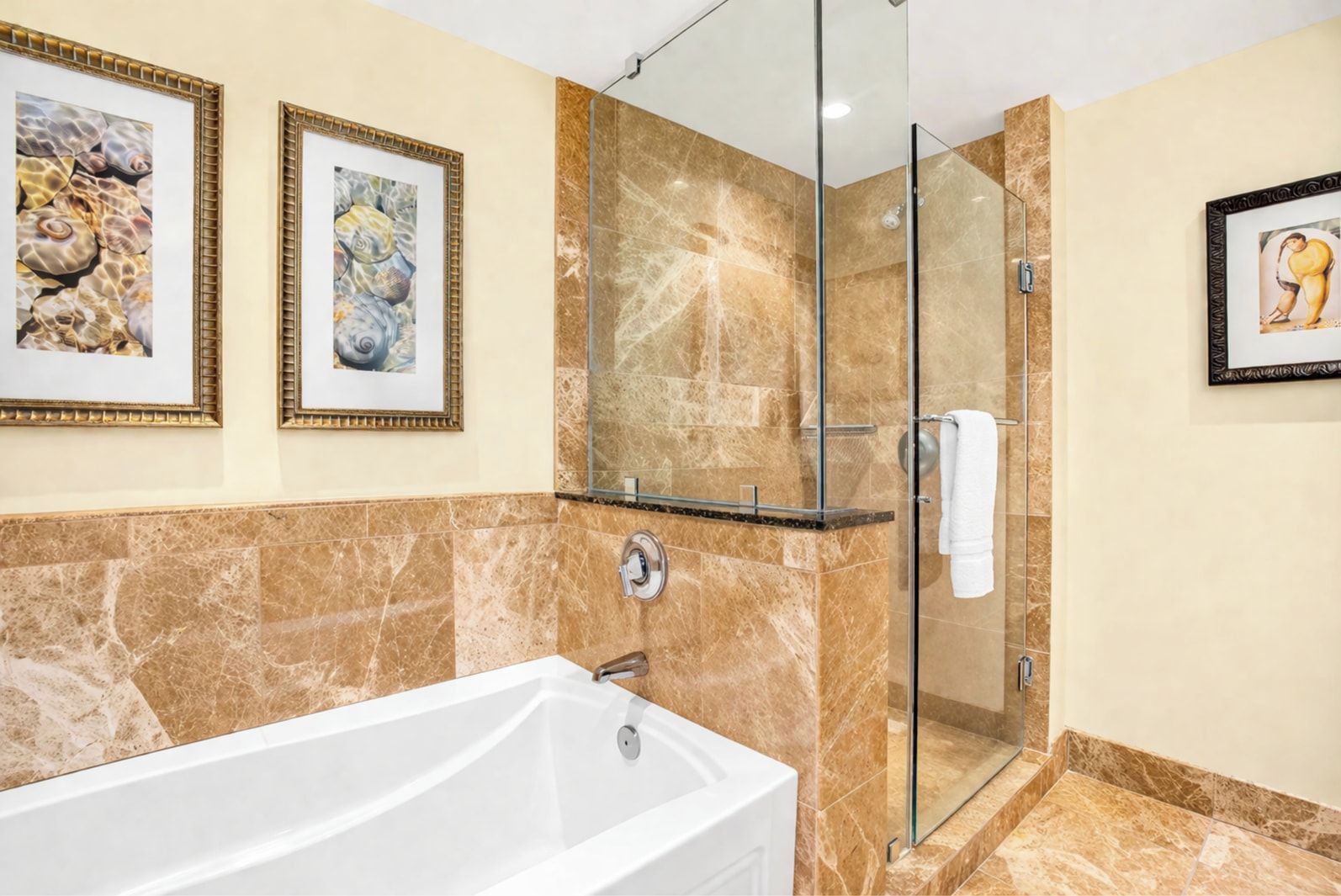 Un baño moderno con bañera, cabina de ducha de cristal y cuadros enmarcados en las paredes.