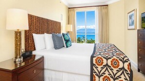 Une chambre d’hôtel avec un lit, des lampes de chevet, une commode et une fenêtre donnant sur l’océan.