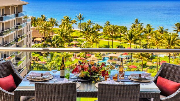 Un balcon avec une table dressée pour le dîner, donnant sur une piscine et des palmiers.