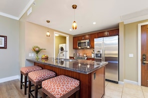 A kitchen with a central island, stainless steel appliances, and a seating area with patterned cushions. - Honua Kai | Ocean View 7 BR, Sleeps 20 | Car Incl. w/ 6+ Nights | HKK ML-3915 by KBM (Lahaina)