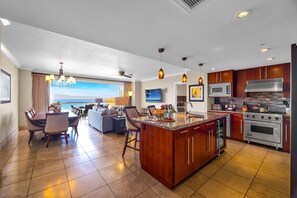 A modern kitchen with a large island, a dining area with a view, and a living room with a sofa and coffee table. - Honua Kai | Ocean View 7 BR, Sleeps 20 | Car Incl. w/ 6+ Nights | HKK ML-3915 by KBM (Lahaina)