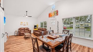 Ein geräumiges Wohnzimmer mit Holzboden, einem Esstisch mit Stühlen, einem Kamin und einem Deckenventilator.