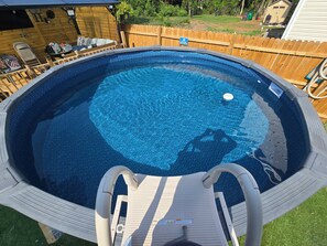 En oval, fristående pool med en träplattform och en säkerhetsstege.