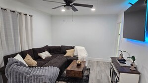 Un soggiorno moderno con un divano componibile, un tavolino da caffè, una ventola a soffitto e una TV a parete.