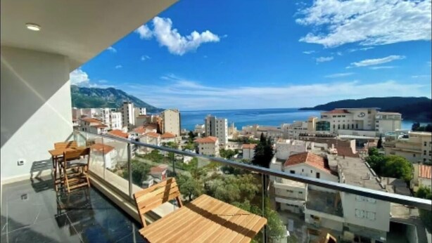 A balcony with a view of a coastal cityscape, including buildings and a mountain range. - Residance with pool ,sauna and free garrage (Budva)