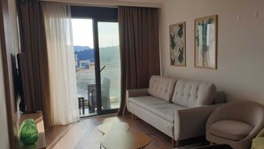 A living room with a sofa, a chair, a small table, a TV, and a sliding glass door leading to an outdoor area. - Residance with pool ,sauna and free garrage (Budva)