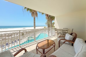 A balcony with a view of the beach, a pool, and wicker furniture. - Admirals Quarters 204 | Beachfront Views | Indoor & Outdoor Pools | My Beach Getaways (Orange Beach)