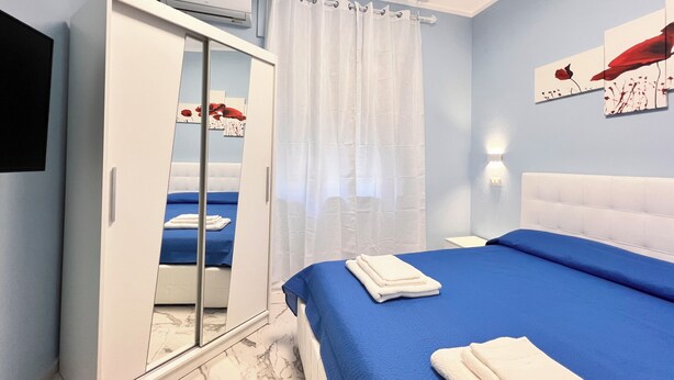 Ein Schlafzimmer mit Bett, Kleiderschrank, Spiegel, Flachbildfernseher und Wandleuchte.