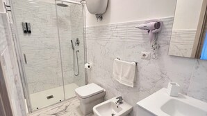 Ein modernes Badezimmer mit Duschkabine aus Glas, einem Bidet, einem Waschbecken und einem Spiegel.