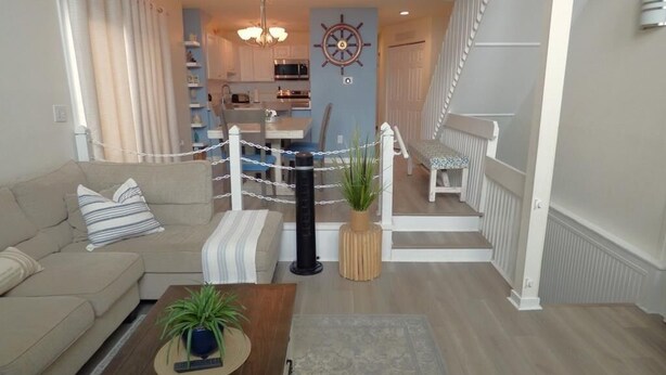 A living room with a sofa, a coffee table with a plant, a rug, a kitchen area with cabinets, a dining table, and a staircase. - Charming Family Retreat Near Beach & Boardwalk, 841 Plymouth Place (Ocean City)